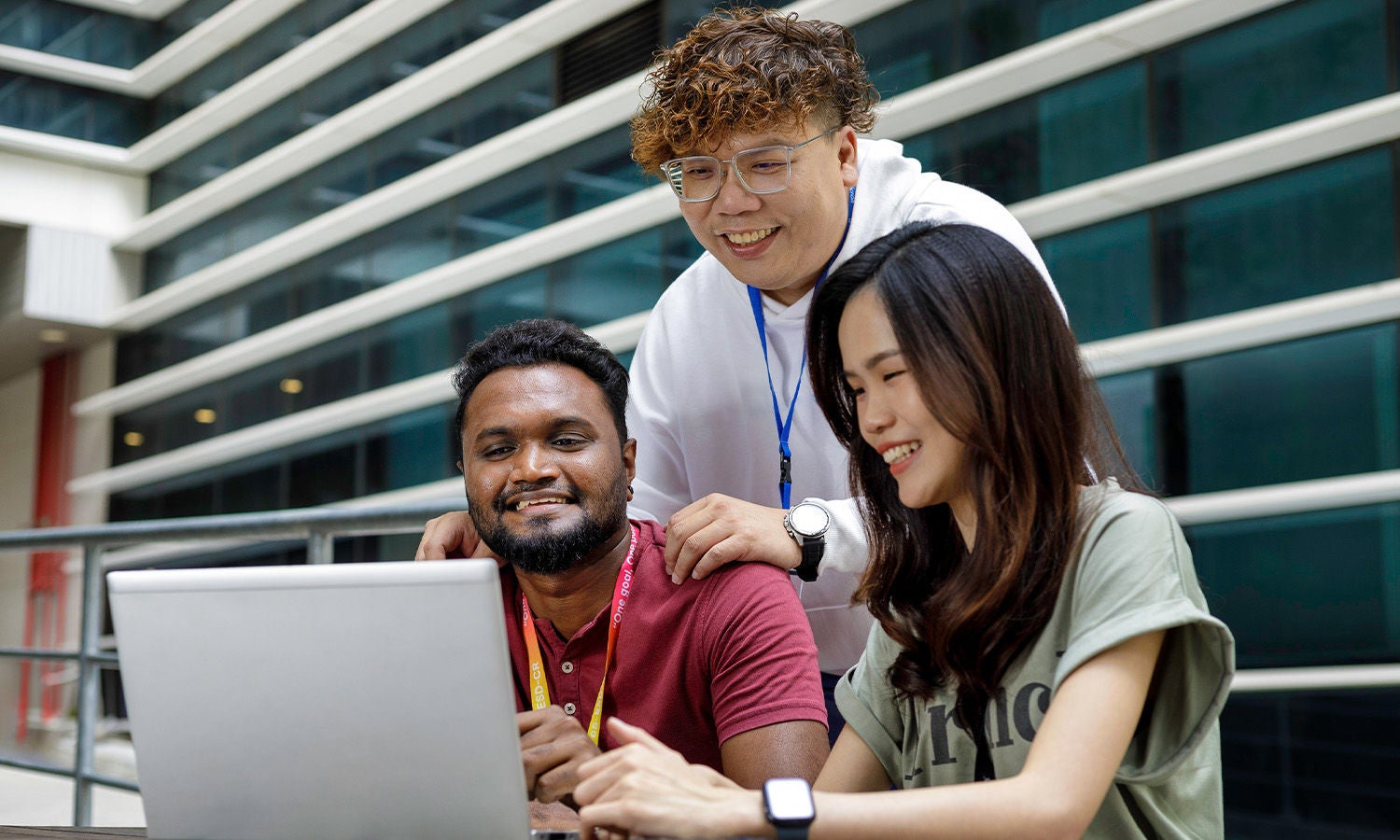 Three smiling Micron employees collaborating at a laptop in a modern workspace